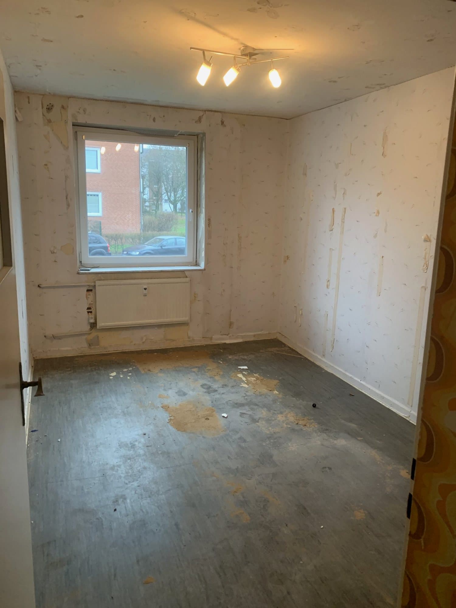 Zimmer nach der Räumung: Tapetenreste und alter Bodenbelag