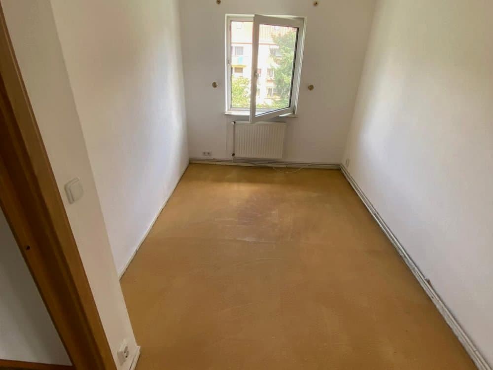 Leeres, schmales Zimmer mit hellem Boden und Fenster